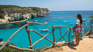 Eine Urlauberin genießt den Ausblick auf die türkise Bucht von Cala Macarella