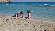 Kinder bauen vor glasklarem Wasser eine Sandburg am Strand